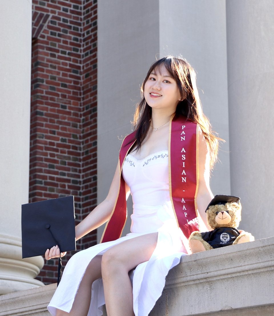 Yanqi Luo at Harvard commencement, holding her mortarboard and wearing a Pan-Asian graduation stole