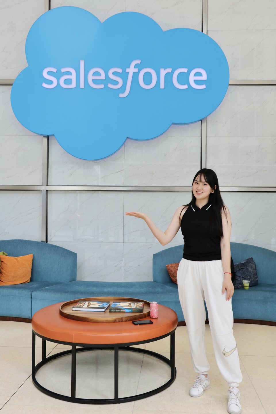 Yanqi Luo in a Salesforce office lobby, beside the Salesforce cloud logo